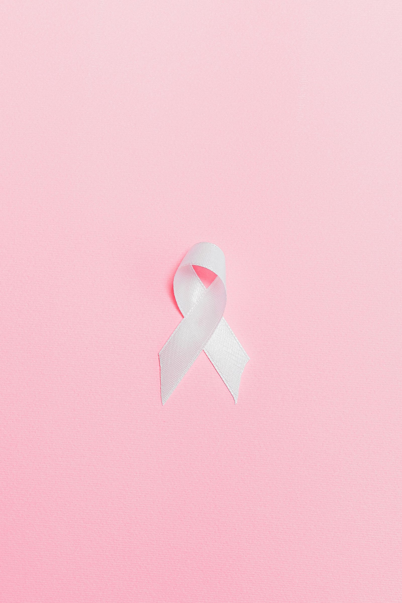 A pink ribbon symbolizing breast cancer awareness set against a light pink background.
