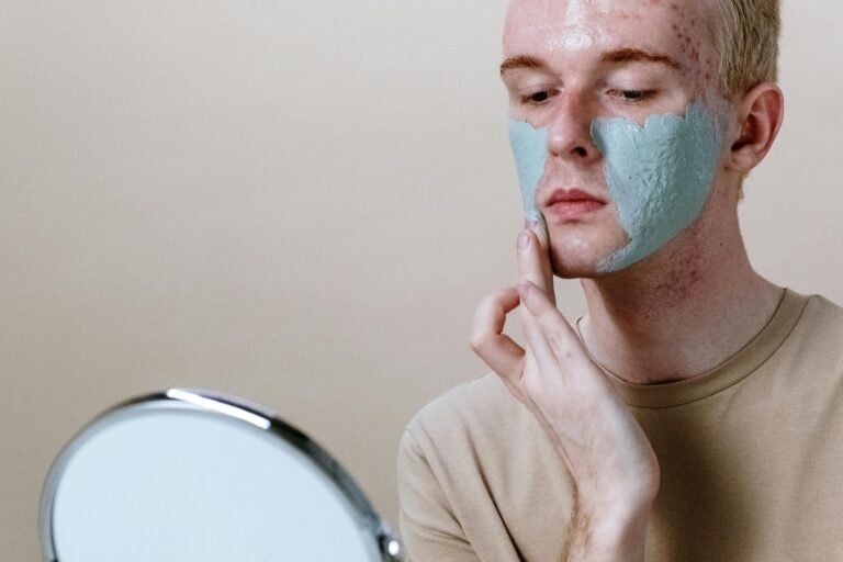 Close-up of a young man applying a clay face mask with a mirror.