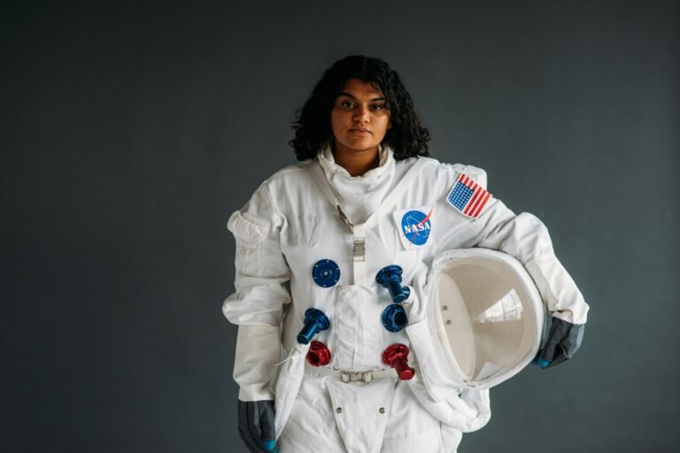 Woman dressed as astronaut holding helmet in NASA suit against grey background.