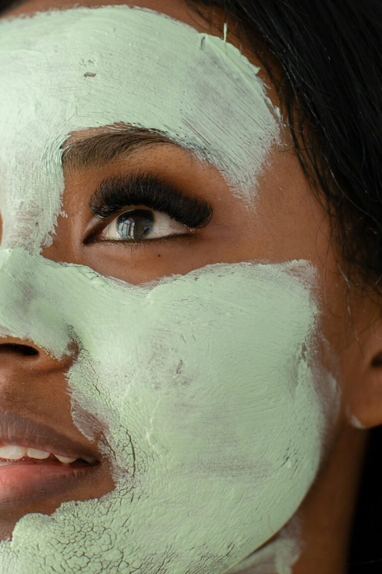 A close-up portrait of a woman with a green clay facial mask focusing on eye detail.