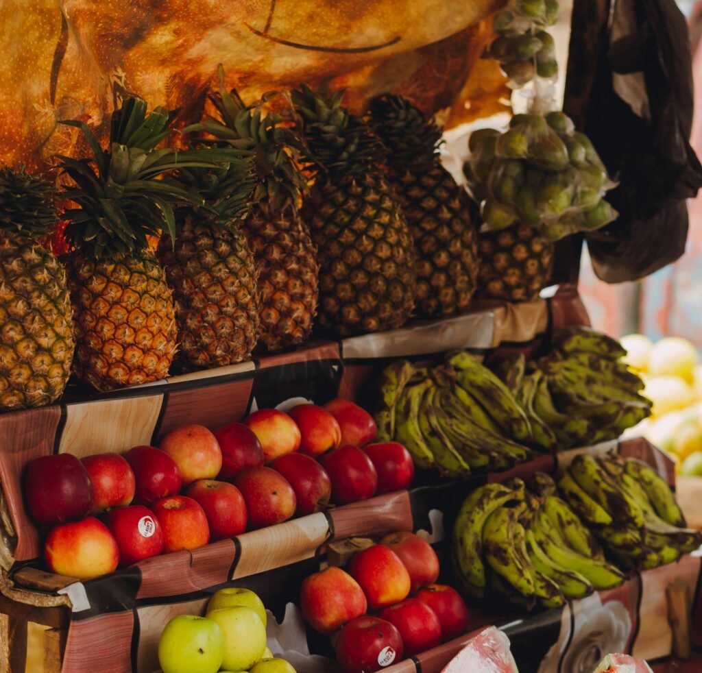 A colorful market stand with pineapples, bananas, and apples arranged neatly under a warm light.