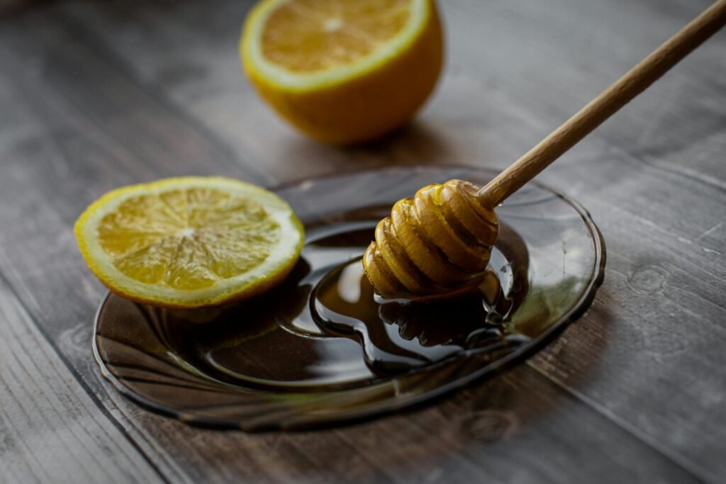 Honey dipper placed on saucer with lemon slice and sweet honey on wooden table